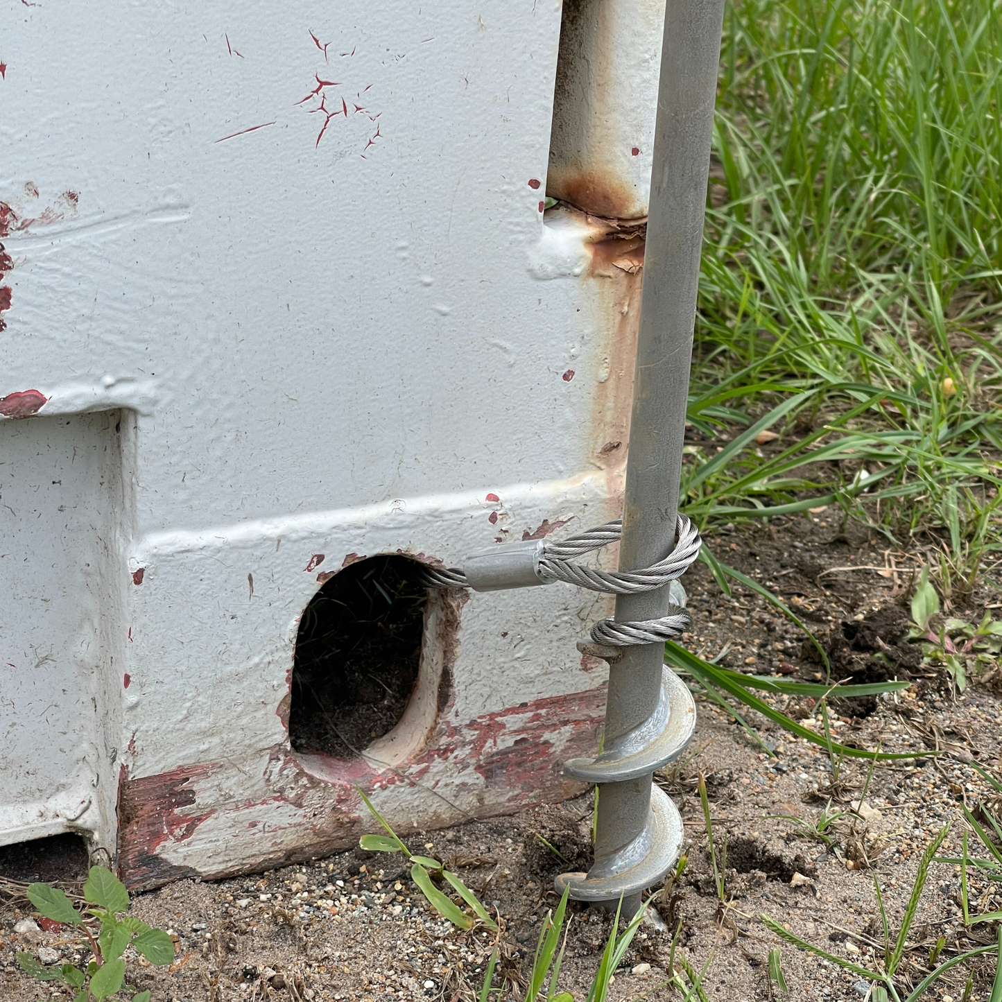 Steel ground anchor with steel cable looped to shipping container