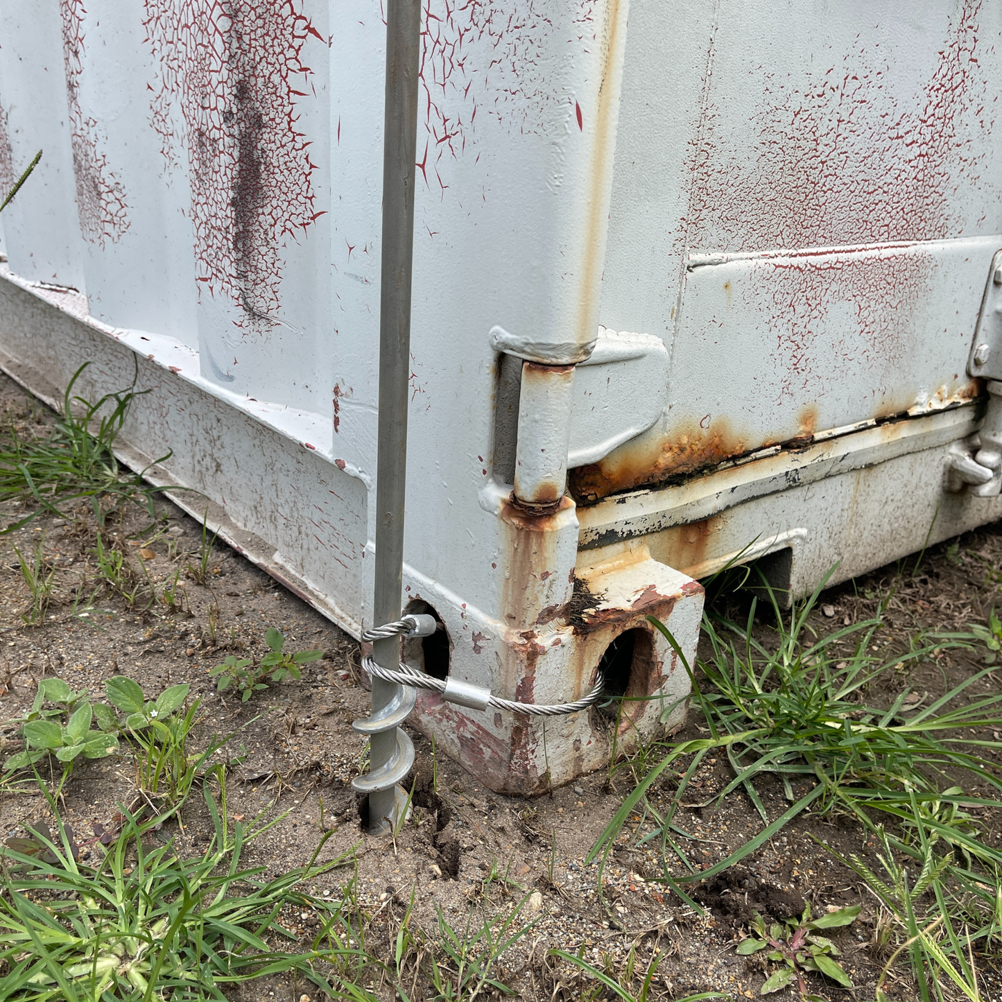 Steel ground anchor with steel cable threaded to shipping container