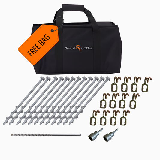 Ground Grabba ground anchoring kit with a black carrying bag, orange free bag tag, multiple gray anchor bolts, brown ground anchors, a drill bit, and two socket tools on a white background.